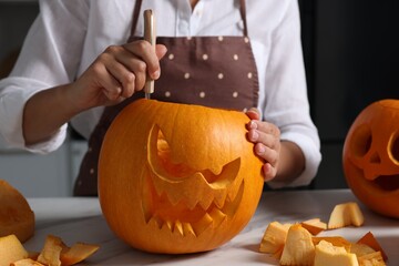 Woman carving pumpkin for Halloween at white marble table, closeup