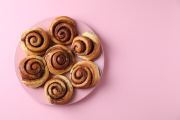 Many tasty cinnamon rolls pink background, top view. Space for text
