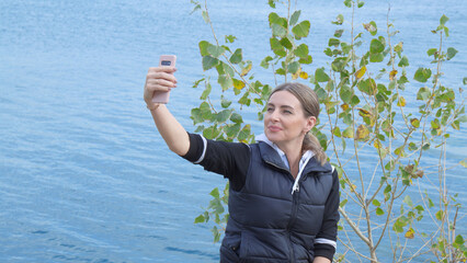 Woman tourist makes video call against backdrop of beautiful nature and lake.