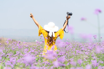Traveler or tourism Asian women standing and raise arm chill with camera in the purple  verbena flower field in vacations time.  People  freedom and relax in the spring  meadow.  Lifestyle Concept