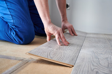 Close up of man construction worker installing laminate timber flooring in apartment under...