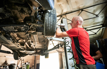 Hardworking, professional worker, repairman changing wheels of car. Man wearing dirty gloves, repairing, fixing car. Concept of repairing, maintaining automobiles.