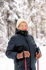 Close-up of a senior elderly woman training Nordic walking with ski trekking poles in a snowy...