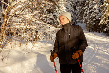 Senior elderly woman training Nordic walking with ski trekking poles in a snowy forest.Active rest...