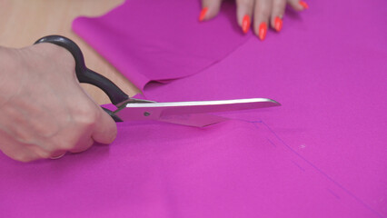 Cutting material for sewing clothes with scissors in sewing workshop.