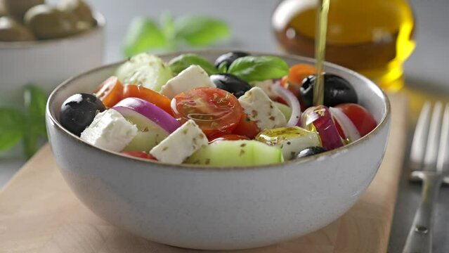 Pouring olive oil into a bowl of traditional Greek salad. Fresh vegetable salad with feta cheese.

