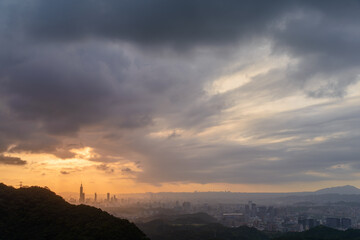 At dusk, the sun breaks through the clouds and shines on Taipei City. Silhouettes of city buildings. Orange sky and dark clouds.