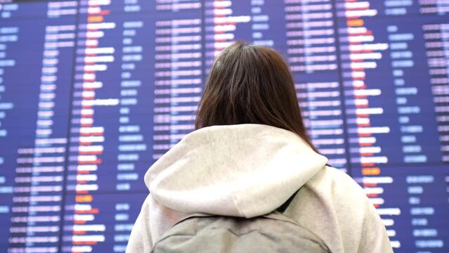 Lady in airport terminal approaches schedule of aircraft flights. Woman searches for right flight for journey and eventually finds correct plane