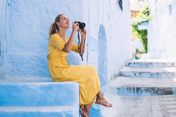 Joyful traveler photographing on camera sitting in street - Powered by Adobe