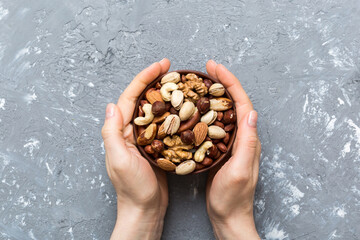 Woman hands holding a wooden bowl with mixed nuts Walnut, pistachios, almonds, hazelnuts and cashews. Healthy food and snack. Vegetarian snacks of different nuts - obrazy, fototapety, plakaty