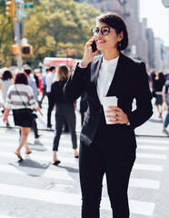 Positive corporate manager talking on phone during coffee break outdoors holding takeaway cup