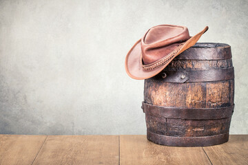 Wild West old retro leather cowboy hat and aged antique oak barrel. Vintage style filtered photo - obrazy, fototapety, plakaty