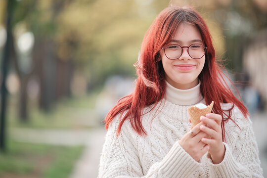 Happy girl in a white sweater holds ice cream in a waffle cone in her hands.