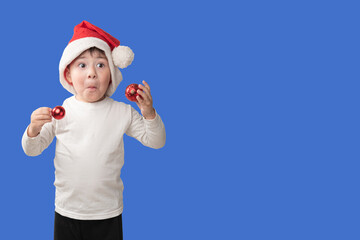 A caucasian boy with a surprised expression wearing a red and white Christmas hat celebrating Christmas on a blue background. christmas concept. copy space.