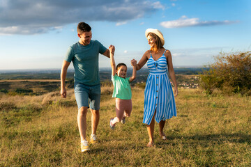 Mother and father are holding their daughter's hands as they walk through the field, having fun and laughing