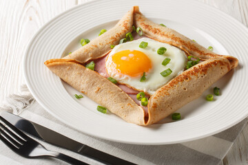 Breton galette, galette sarrasin, buckwheat crepe, with fried egg, cheese, ham closeup on the plate on the table. Horizontal