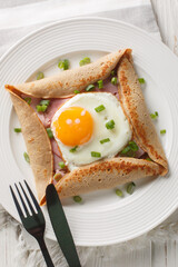 Buckwheat crepe galette with ham and egg for tasty healthy breakfast closeup on the plate on the table. Vertical top view from above