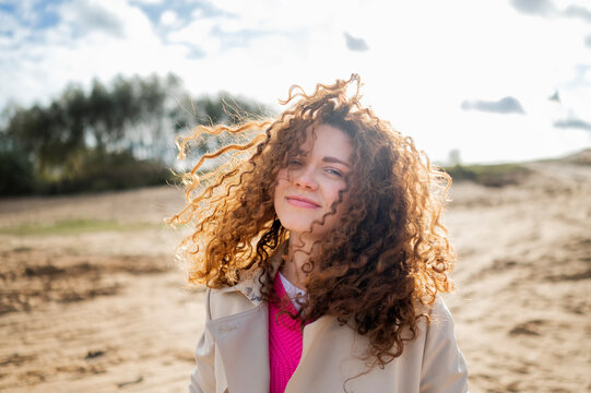 Smiling woman with curly hair standing on sand at beach