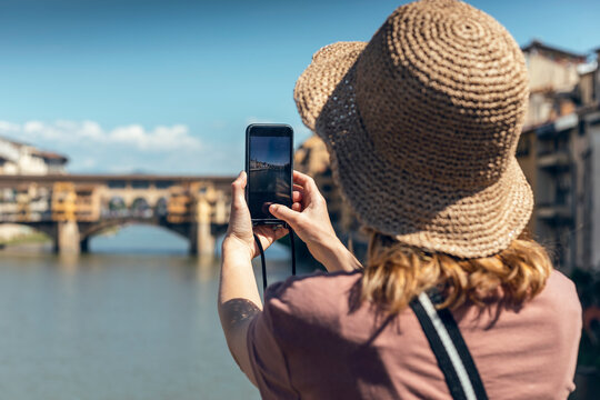 Tourist wearing hat photographing Ponte Vecchio over Arno River