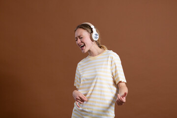 Woman imitating guitar and enjoying music on headphones against brown background