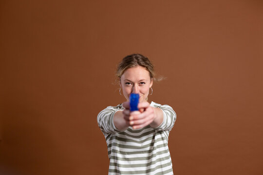 Blond woman holding toy gun over brown background