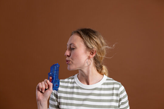 Blond woman blowing toy gun against brown background in studio