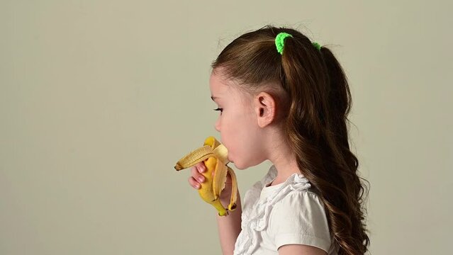 Happy little girl bites and eats banana, fruit and baby.