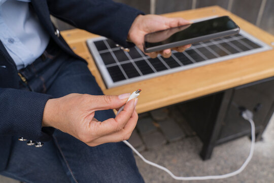 Businesswoman plugging USB cable in smart phone at solar charging point