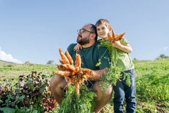 Boy with arm around father holding carrots in vegetable garden