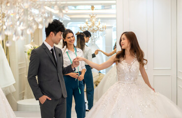 Portrait of smiling happy love asian couple fashion groom man and bride woman talk and try on wedding dress with woman shop owner for pre wedding at wedding interior fashion studio