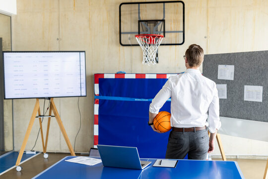 Businessman Standing With Basketball In Front Of Hoop And Device Screen