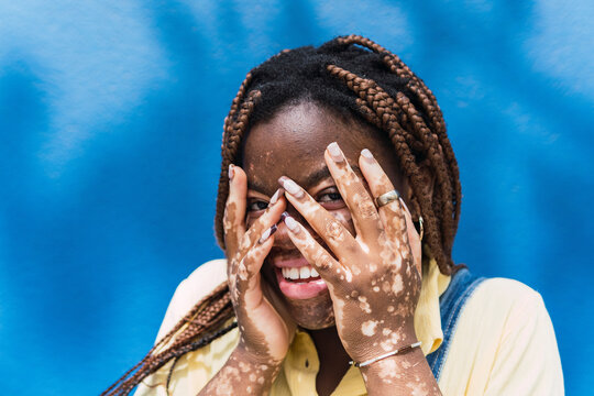 Happy Young Woman Covering Face In Front Of Blue Wall