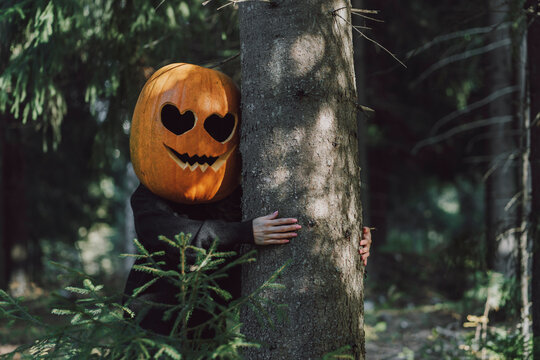 Woman wearing Jack O' Lantern and hugging tree in forest