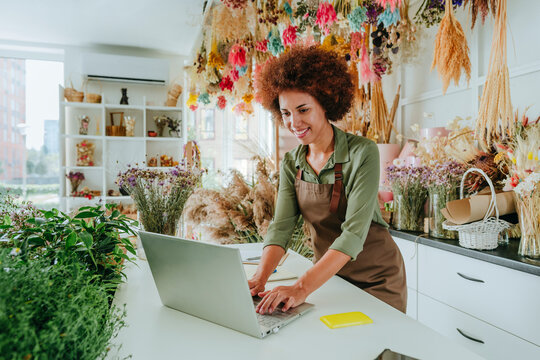 Smiling young Afro store owner using laptop at desk in flower shop