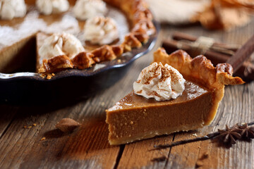 Pumpkin pie with whipped cream and cinnamon on wooden background

