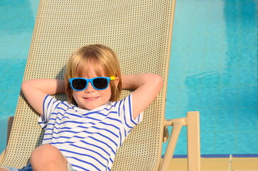 Cute boy relaxing in a sun lounger near the pool at the hotel. Family vacation, child in...