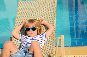 Cute boy relaxing in a sun lounger near the pool at the hotel. Family vacation, child in...