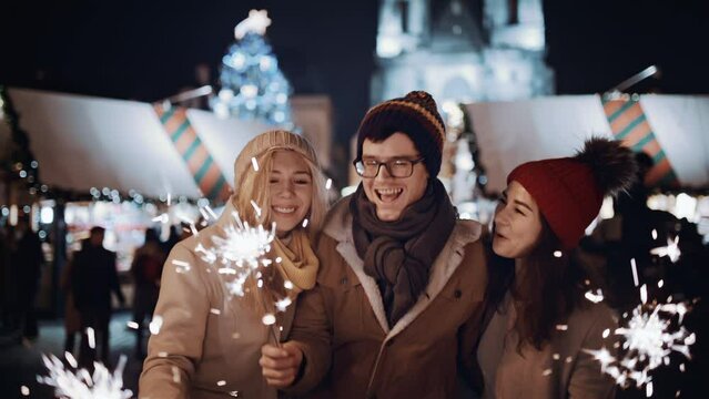 Two women and man smiling waving firework express joy happiness. Christmas holiday. Multiracial group of friends having fun with sparklers outdoor celebrating merry Christmas xmas and happy new year.