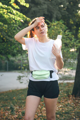 Tired young woman with a bottle of water in the park after a run.