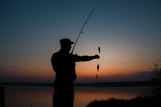 A fisherman silhouette fishing at sunset. Freshwater fishing, catch of fish. High quality photo