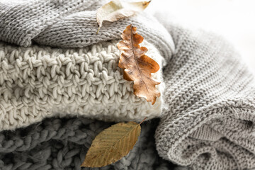 Close-up of a stack of knitted sweaters with autumn leaves.