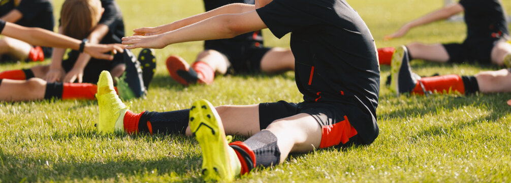 School kids stretching on the grass sports pitch. Group of soccer football players in black soccer jersey shirts stretching their legs after the training game. Sports team in outdoor practice