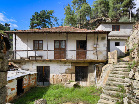 Pequeno bairro abandonado com algumas casas velhas e umas escadas em pedra de granito com um pinheiral ao fundo em Portugal