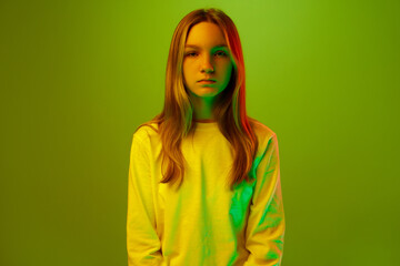Portrait of one calm pretty little girl dressed casually against green studio background in mixed neon light, filter.