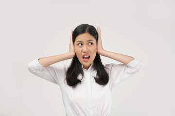 Portrait of a young Asian woman worried overthinking and panicking with hands on ears under pressure. Wearing a white shirt and isolated on a white background.