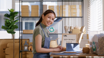 Eco friendly packaging in net zero waste store asian seller retail home office shop. ESG startup Small SME owner young adult woman asia people happy vendor smile carry parcel postal looking at camera.