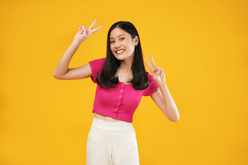 Photo of a young Asian woman carefree showing peace or enjoying life, smiling broadly, isolated on a yellow background.