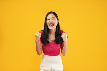 Photo of a cheerful young Asian woman her hands clenched into fists and a happy smile, isolated on...