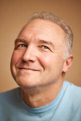 Obraz premium Close-up portrait of smiling middle aged man looking away isolated beige studio background.