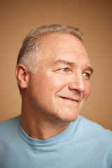 Fototapeta premium Close-up portrait of smiling middle aged, 45s man looking away isolated beige studio background.